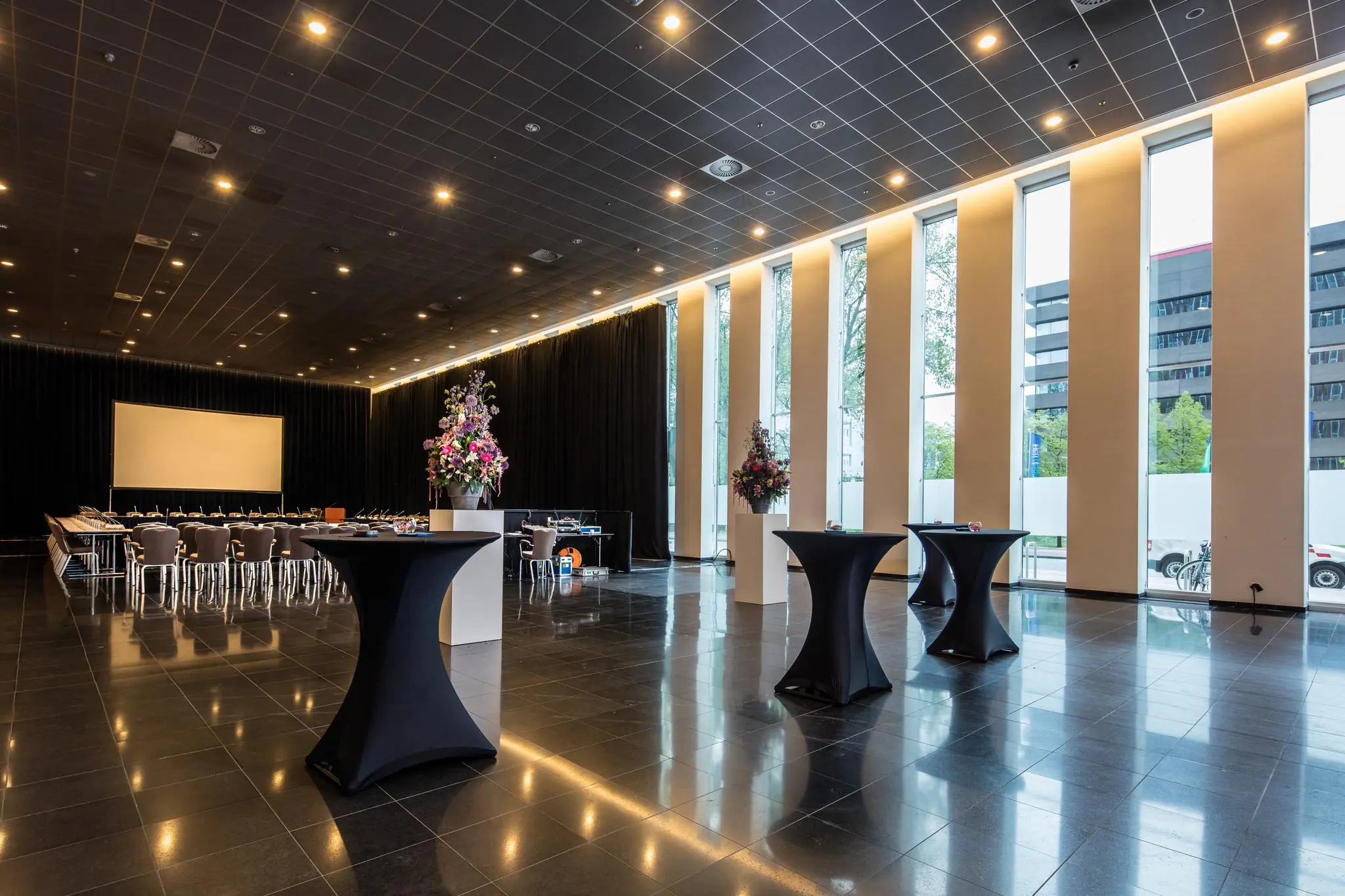 Moderne vergaderruimte aan de Prinses Beatrixlaan met hoge ramen, sta-tafels en een grote opstelling met scherm.